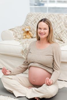 Pregnant woman doing yoga on the floor and smiling at the camera