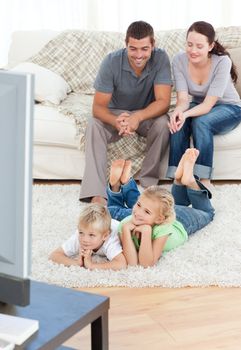 Adorable siblings watching television with their parents lying on the floor in the living-room