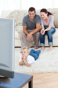 Cute little boy watching television on the floor with his parents in the living-room