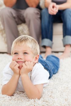 Cute little boy lying on the floor and watching television with his parents at home