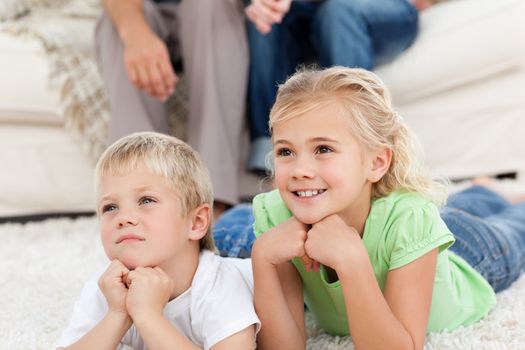 Brother and sister watching television on the floor with their parents in the living-room