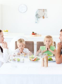 Parents and their children praying during their lunch in the kitchen