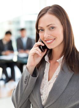 Happy businesswoman on the phone while her team is working in the background