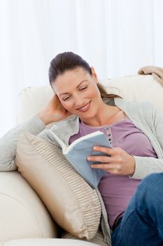 Cute woman reading a romance sitting on the sofa at home