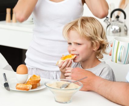 Serious boy eating a toast with marmalade during breakfast with his family