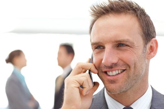 Handsome businessman on the phone while his partners standing on the background