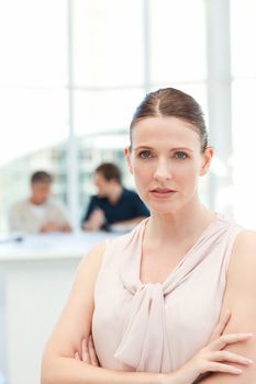 Serious businesswoman looking at the camera while her coworkers are talking in the office