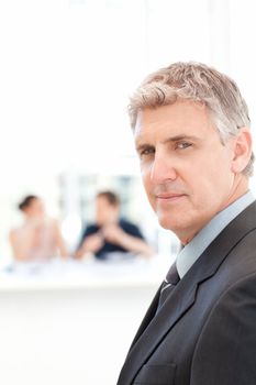 Businessman looking at the camera while his team is working in the background