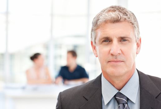 Businessman looking at  the camera while his team is working in the background
