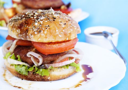 Burger with meat and baked vegetables on a blue background