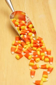 A scoop of candy corn spilling on a wood texture.