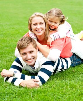 Good looking man lying on his belly with his wife and daughter on top of him