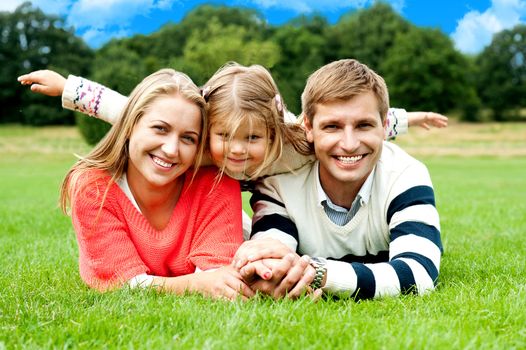 Couple lying in park with their daughter on top. Daughter stretching her hands sideways