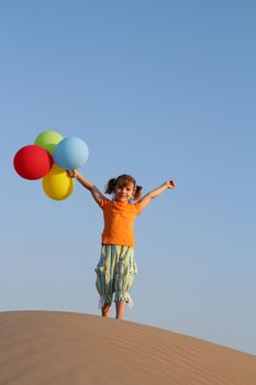 happy little girl with balloons standing on sand dune