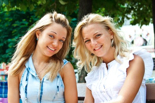 Two beautiful young woman resting on a bench in the park after shopping