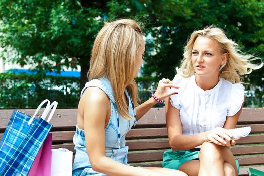 Two beautiful young woman resting on a bench in the park after shopping