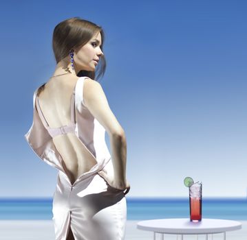 back of rich woman that is unbuttoned dress on sea shore with a glass of cocktail