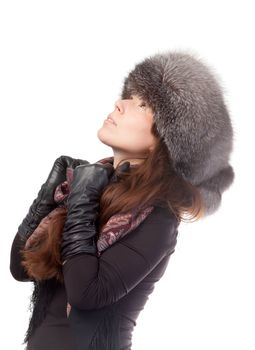 Elegant fashionable woman in winter outfit wearing a scarf, leather gloves and warm fur hat looking up into the sky deep in thought