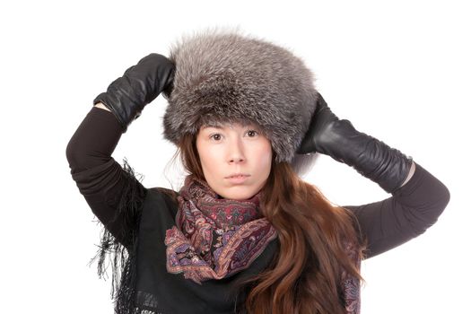 Glamorous woman in winter fashion standing with her gloved hands raised to her fur hat isolated on white