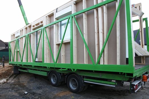 Delivery of the various sections of a prefabricated wooden house witth the exterior walls loaded onto a long bed industrial trailer for transportation