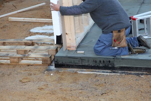 Builder installing a prefabricated exterior wall of a timber frame newbuild house onto a cement foundation