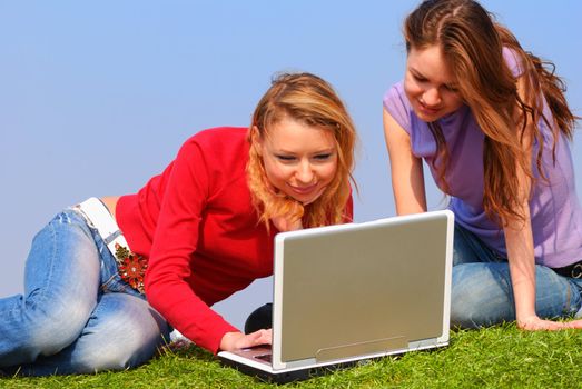 Girls with notebook sitting on grass against sky                                      