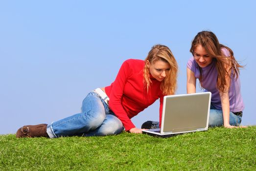Girls with notebook sitting on grass against sky                                      