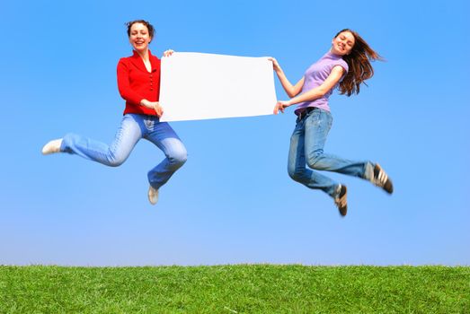 Girls jumping with blank sheet against blue sky