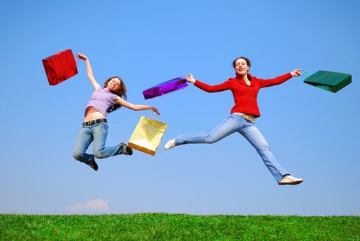 Girls jumping with bags against blue sky