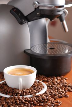 Coffee machine and cup of espresso. Spilled out coffee beans.