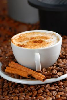 Cup of cappuccino  with cinnamon and spilled out coffee beans.