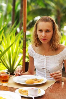 Girl is eating breakfast. Palms in background.