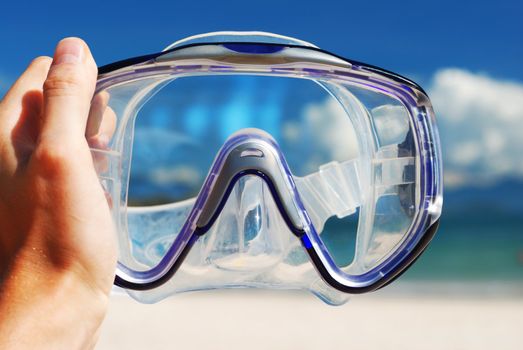 Snorkel equipment in hand against beach and sky