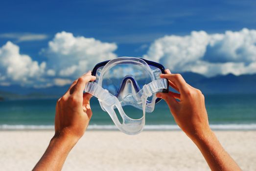 Snorkel equipment in hands against beach and sky