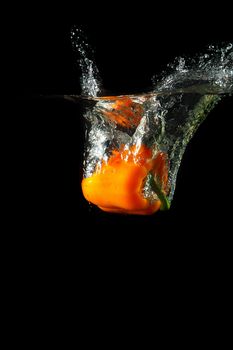 Colored orange paprika in water splashes on black background