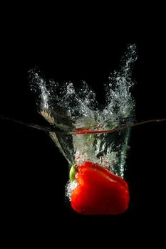 Colored red paprika in water splashes on black background