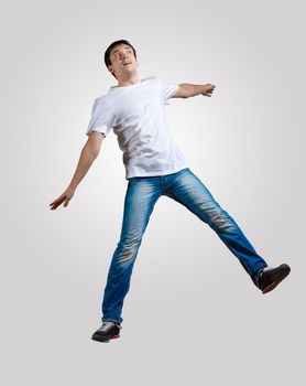 Modern slim hip-hop style man jumping dancing on a grey background