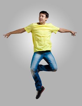 Modern slim hip-hop style man jumping dancing on a grey background