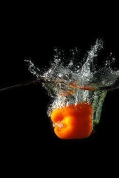 Colored orange paprika in water splashes on black background