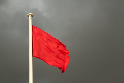 A white flag pole with a bright red flag against a grey cloudy sky.