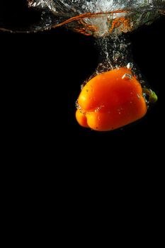 Colored orange paprika in water splashes on black background