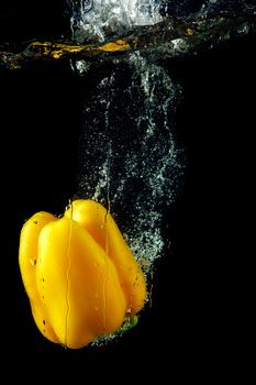 Colored yellow paprika in water splashes on black background