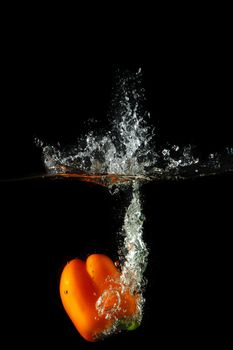 Colored orange paprika in water splashes on black background