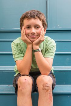 young boy in green on blue steps with scrapped knees