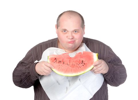 Obese man with a serviette bib around his neck standing eating a large slice of fresh juicy watermelon isolated on white