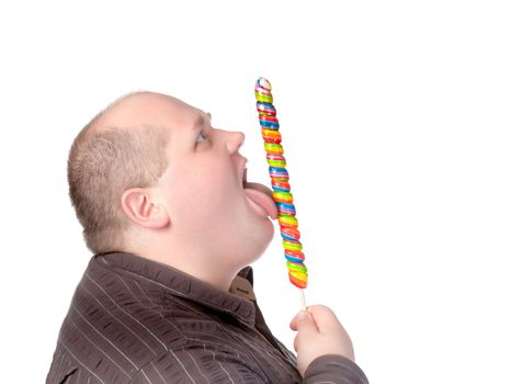 Fat obese man enjoying a a long colourful striped lollipop, standing licking it with a look of complete absorption totally oblivious to his surroundings