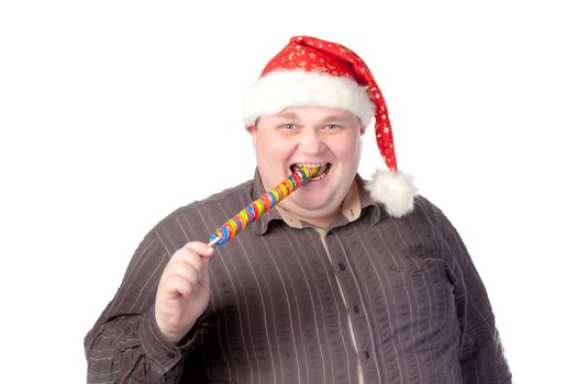 Cheerful obese man in a red Santa hat chewing on a long colourful spiral lollipop with a grin on his face isolated on white