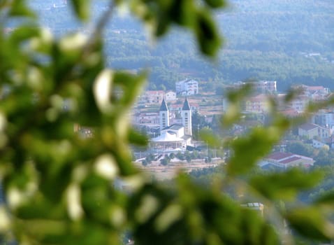 Saint James church and the town of Medjugorje in Bosnia - Herzegovina, as seen through a tree on Krizevac Mountain.