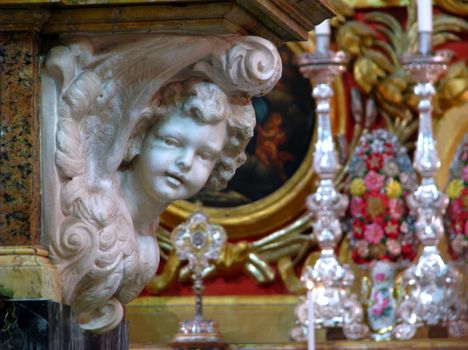 A marble angel with silver chandeliers in the background in Zejtun, Malta.