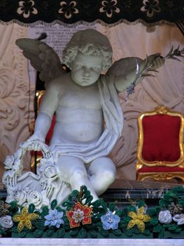 A marble statue of an angel in a church in Valletta carrying a basket full of flowers.